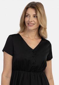 Rochie neagră până la genunchi, cu mâneci scurte, decolteu în V, detalii cu nasturi și o talie elastică pentru o ajustare relaxată. Textură satinată netedă.