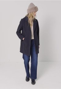 Granatowy wełniany płaszcz o dopasowanej sylwetce, zestawiony z szerokimi dżinsami i beżową wełnianą czapką z futrzanym wykończeniem. W komplecie czarne botki za kostkę.