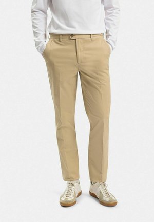 Beiga chinos i en skräddarsydd passform med flat front, två sidofickor och en bakficka. Matchas med vita och grå sneakers.