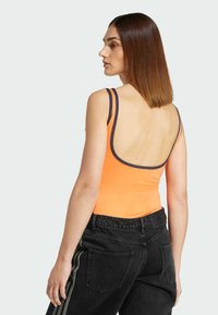 Oranje tanktop met smalle bandjes en een lage rug, gecombineerd met zwarte high-waisted jeans met zijkanten en een textuurafwerking.