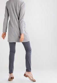 Tunique grise à manches longues avec une coupe droite, associée à un jean skinny gris foncé. Les chaussures sont légères avec des accents rose pâle et doré.