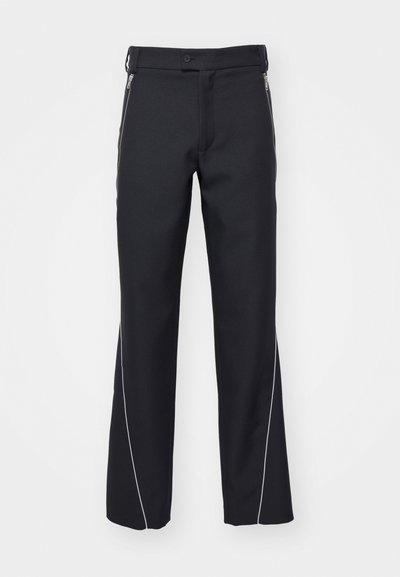 Pantalons noirs en matériau lisse, avec une coupe droite, des poches zippées sur les côtés et des passepoils blancs le long des coutures.