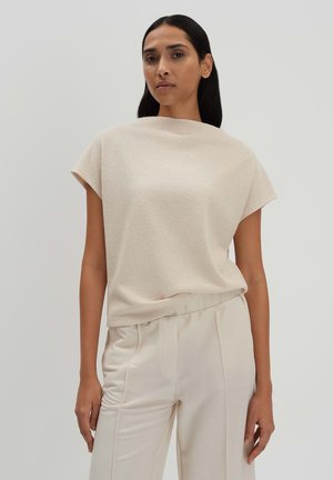 Beige short-sleeve top with a relaxed fit. Textured fabric, high neck, and smooth finish. Paired with light beige tailored pants.