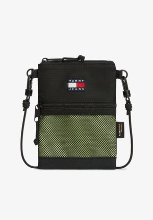 Piccola borsa a tracolla nera con tasca frontale in rete verde, logo Tommy Jeans, etichetta in tessuto Cordura e tracolla regolabile con clip.