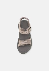 Brune og grå sandal med justerbare stropper, polstret fotseng og en teksturert gummisåle. Har to spenne-lukkinger for tilpasning av passform.
