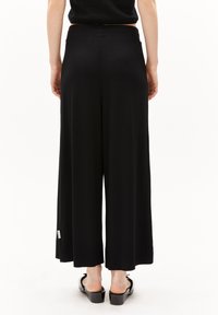 Zwarte wijde broek van zachte stof met een elastische tailleband. Heeft een subtiel zijkenteken en een gladde textuur.
