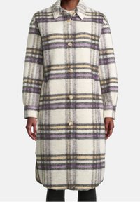 Abrigo largo de lana de cuadros con cierre de botones en tonos de crema, púrpura, gris y beige, llevado sobre pantalones negros.