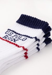Calzini bianchi con strisce blu navy e rosse, caratterizzati da polsini a coste e con "U.S. POLO ASSN." ricamato in blu navy sul lato. Tessuto morbido.