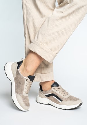 Beige Sneaker mit strukturiertem Obermaterial aus Wildleder und Leder, schwarzen Akzenten, weißer Sohle und runden Schnürsenkeln. Die Hose hat eine gerippte Struktur.