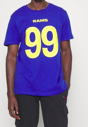 Hombre con una camiseta azul de los Rams con un gran número amarillo 99 y pantalones negros con un bolsillo lateral.