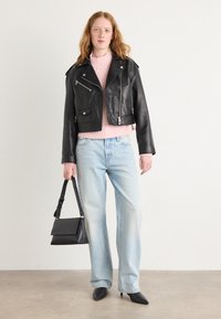 Black leather biker jacket with zippers, light pink knitted sweater, light blue wide-leg jeans, and pointed black heels, holding a black handbag.