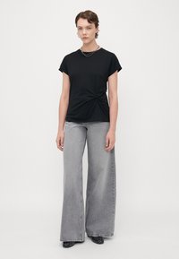 Svart knuten t-shirt med korta ärmar, i kombination med högmidjade, vida grå jeans och svarta spikiga klackar. Enkelt mönster och avslappnad passform.