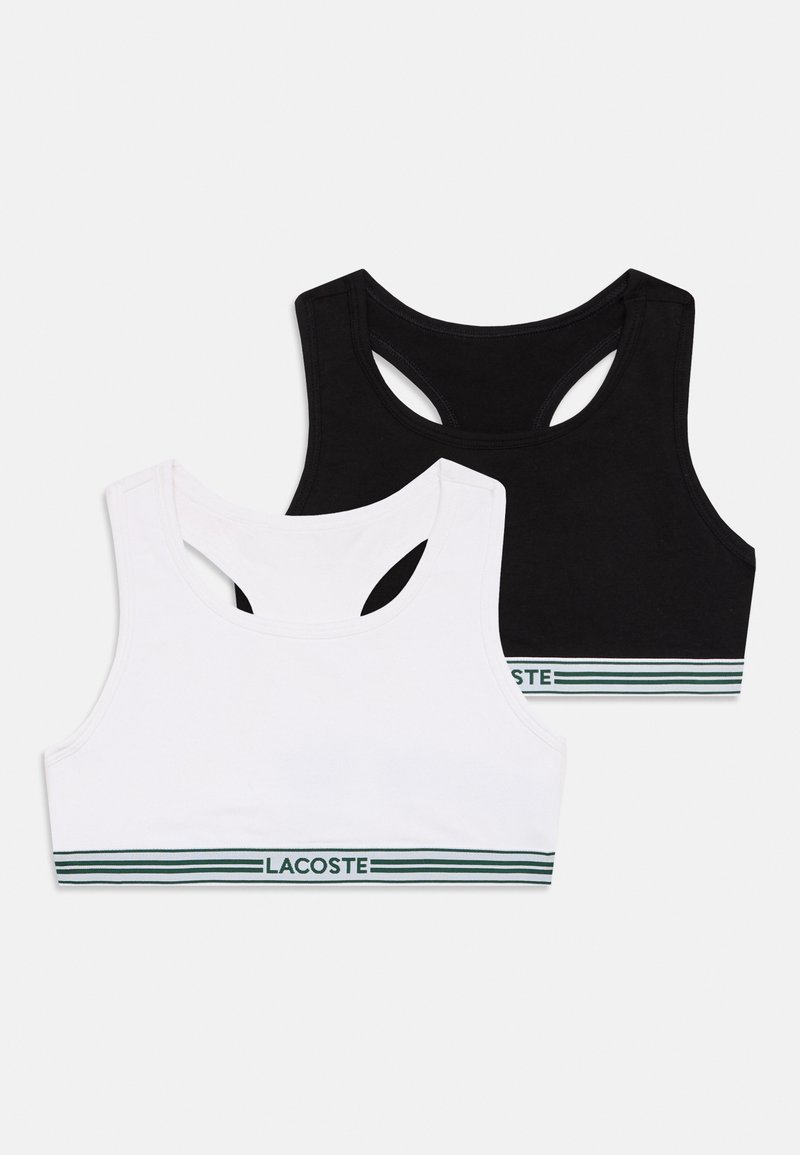 Dois soutiens desportivos de algodão, um preto e um branco, com decote redondo e design de costas nadador. Ambos possuem faixas elásticas com riscas verdes.