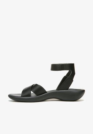 Black leather sandal featuring crisscross straps, ankle support, and a curved sole design for comfort. Smooth texture with a minimalist look.
