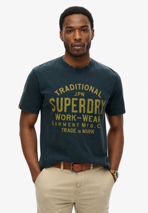 Mørkeblå bomulds T-shirt med rund halsudskæring og korte ærmer, med fedt gult tekst "SUPERDRY" og "WORK-WEAR" i et stort skriftmønster.