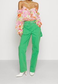 Květinová off-shoulder blůza v růžové, oranžové a zelené barvě s volány; spárovaná s jasně zelenými širokými kalhotami a bílými vysokými podpatky.