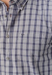 Marineblauwe en witte geruite shirt met een button-down kraag, voorzien van een borstzak en een textuurstof. Twee knopen zichtbaar op de kraag.