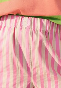 Różowe i kremowe, pionowo paskowane szorty z elastycznym pasem z małym białym haftowanym logo pod brzoskwiniową i zieloną bluzką.