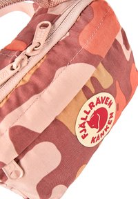 Κοντινό πλάνο μιας τσάντας Fjällräven Kånken με ροζ και καφέ καμουφλάζ σχέδιο, με ορατά φερμουάρ και στρογγυλή ετικέτα με το λογότυπο της μάρκας.