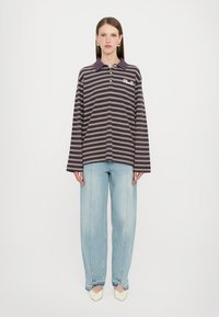 Polo de manga larga en púrpura oscuro con franjas horizontales blancas, características de un cuello con solapa y detalle de logo. Combinado con jeans azul claro.