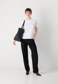 White T-shirt with blue graphic, paired with black wide-leg pants and black pointed-toe heels. Black tote bag with a smooth texture.