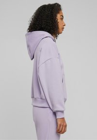 Sweat-shirt à capuche lavande clair avec une coupe décontractée, des poignets côtelés et une poche kangourou. Texture douce avec un léger éclat.