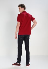 Red polo shirt, dark jeans, and red sneakers. The polo has short sleeves and a collar. The jeans are slim fit with standard back pockets.