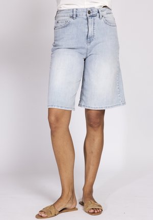 Light blue denim knee-length shorts worn with tan slip-on sandals on a person standing against a plain background.