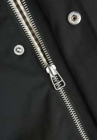 Primo piano di un tessuto nero con una cerniera argento e un bottone a pressione. La cerniera ha una fodera interna decorata con righe.