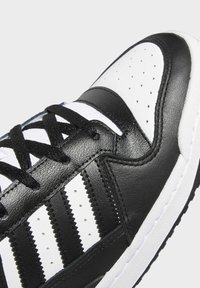 Close-up of black and white sneaker with black laces, perforated toe box, and three black stripes on the side.