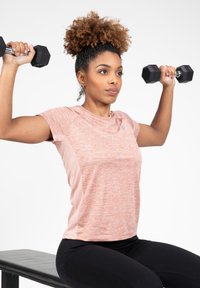 Korte mouwen, roze en grijs sporttop met een gladde textuur, gedragen door een persoon die zwarte dumbbells op een bank tilt.