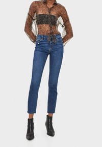 Blusa transparente con estampado de leopardo, de mangas largas y diseño con lazada en el frente, combinada con unos jeans de mezclilla azul de cintura alta y botas negras hasta el tobillo.