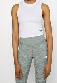 White crop tank top with a round neckline, paired with green textured leggings featuring a logo on the thigh.