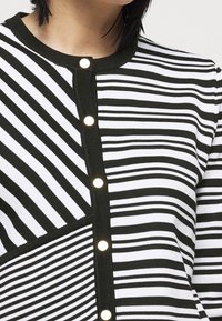 Black and white striped cardigan featuring a button closure, contrasting texture, and geometric patterns with varying widths of stripes.