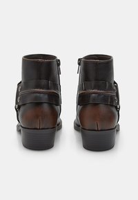 Botas de tobillo de cuero negro con acentos marrones, que incluyen una cremallera lateral, detalle de correa y puntera redonda. Tacón plano y suela texturizada.