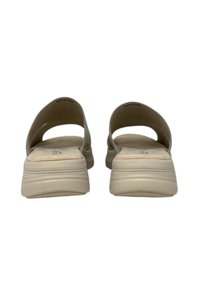 Le ciabatte beige senza chiusura presentano un design curvo, con retro aperto e una soletta texturizzata con un tacco basso. Sono realizzate in materiale flessibile.