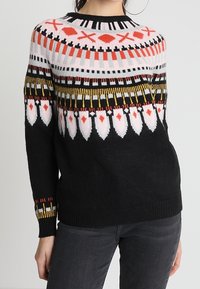 Sweter dzianinowy z czarnym przodem, ozdobiony kolorowymi, geometrycznymi wzorami w kolorach czerwonym, białym i żółtym, z prążkowanym dekoltem i mankietami.