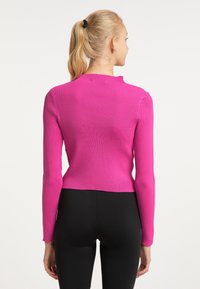 Illeszkedő, rózsaszín bordás pulóver hosszú ujjakkal és magas nyakkivágással, fekete leggings-szel párosítva, amely kiemeli a crop fazont.