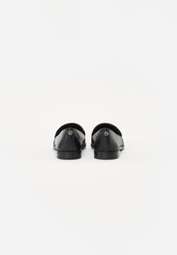 Sorte lærloafers med en glatt tekstur, avrundet tupp, lav hæl og gullaccent bak. Enkel, strømlinjeformet design uten mønstre.