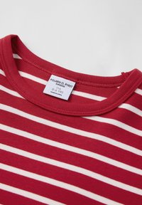 Punainen ja valkoinen raidallinen paita, jossa on pyöreä pääntie ja pehmeä kangas. Tunnuksessa lukee "POLARN O. PYRET, 5-6 VUOTTA, VALMISTETTU KIINASSA."