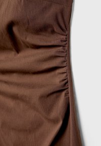 Brunt stof med en glat tekstur, der har samlet detaljering langs den ene side og et simpelt, draperet design.