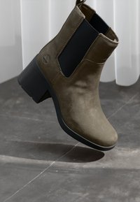 Bottine en daim marron avec un panneau latéral élastique noir, bout rond et épais talon bloc, sur fond neutre.