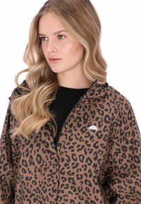 Barna leopárdmintás dzseki kapucnival, fekete cipzárral és egy kis fehér esernyő logóval a mellkason. Sima textúra és könnyű anyag.