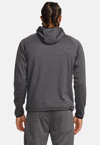 Haut à capuche gris foncé en tissu texturé, avec un capuchon à cordon de serrage et des manches raglan. Assorti avec un pantalon gris.