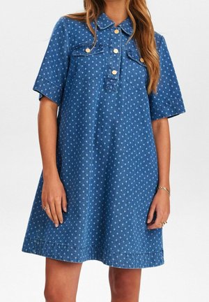 Woman wearing blue short-sleeve denim dress with light blue polka dots, gold buttons, and a collar, shown from neck to mid-thigh.