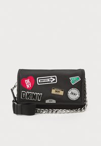 Black nylon crossbody bag featuring various patches, chain accents, and a detachable strap. Displays colorful branding and textured details.