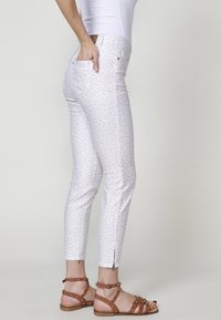 Bijele traperice s uzorkom leopard kože, slim fit, do gležnja, s detaljima na patentnom zatvaraču na rubu. Uparite s smešnim sandalama s zakovicama.