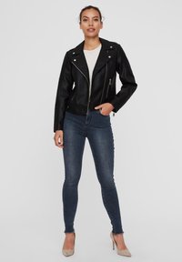 Black leather biker jacket with silver hardware, zippered pockets, and a fitted design, paired with dark blue skinny jeans and beige heels.