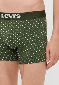 Sötétzöld boxer alsónadrág, fehér 'Levi's' logós derékkal. Világoszöld geometrikus formákkal és pöttyökkel mintázva. Puha, rugalmas anyag.
