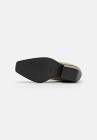 Zapato de tacón de ante beige con suela de goma negra lisa, con puntera redondeada y tacón bajo cuadrado. Sin adornos visibles.